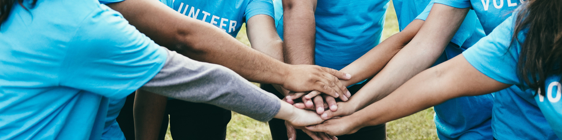 Eine Gruppe Ehrenamtlicher in blauen T-Shirts legt gemeinsam die Hände übereinander.