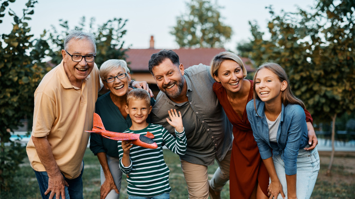 Drei Generationen einer Familie stehen gemeinsam im Garten; ein Junge hält ein Spielzeugflugzeug.