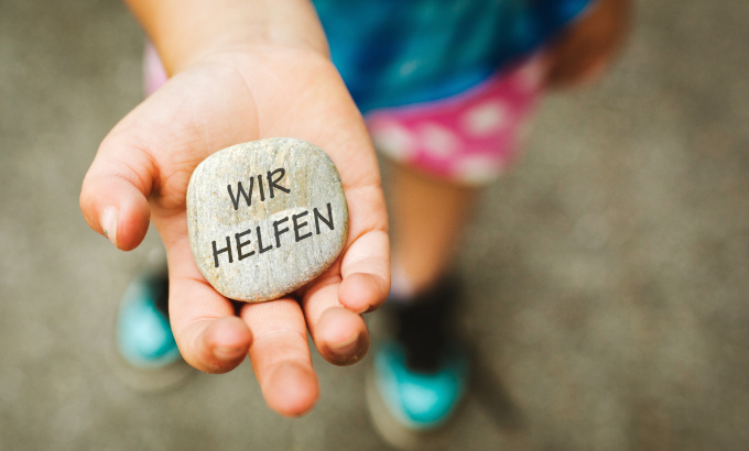 Eine Kinderhand hält einen Stein mit der Aufschrift - Wir helfen.