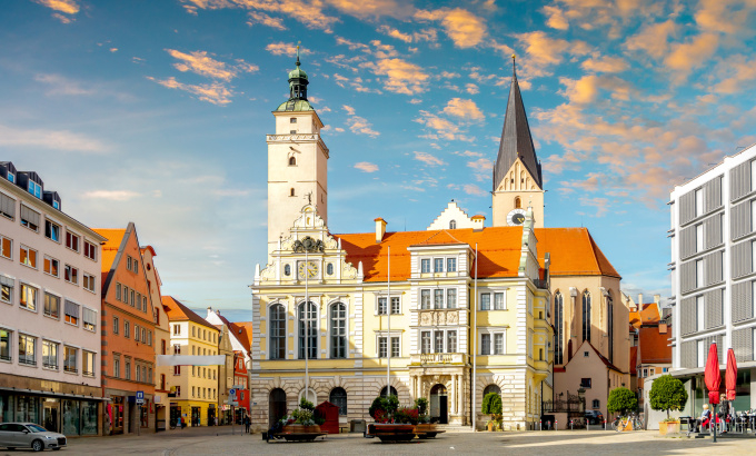 Historisches Rathaus und Kirche an einem sonnigen Stadtplatz unter blauem Himmel.