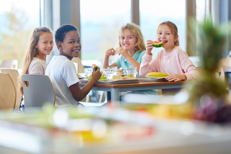 Vier Kinder sitzen gemeinsam an einem Tisch und essen Obst und Brot.