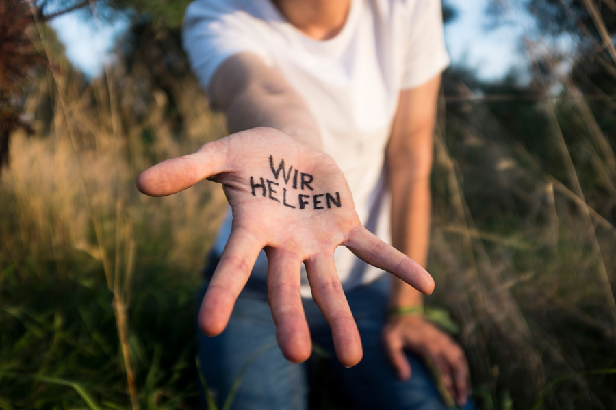 Eine ausgestreckte Hand trägt die Aufschrift Wir helfen auf der Handfläche.