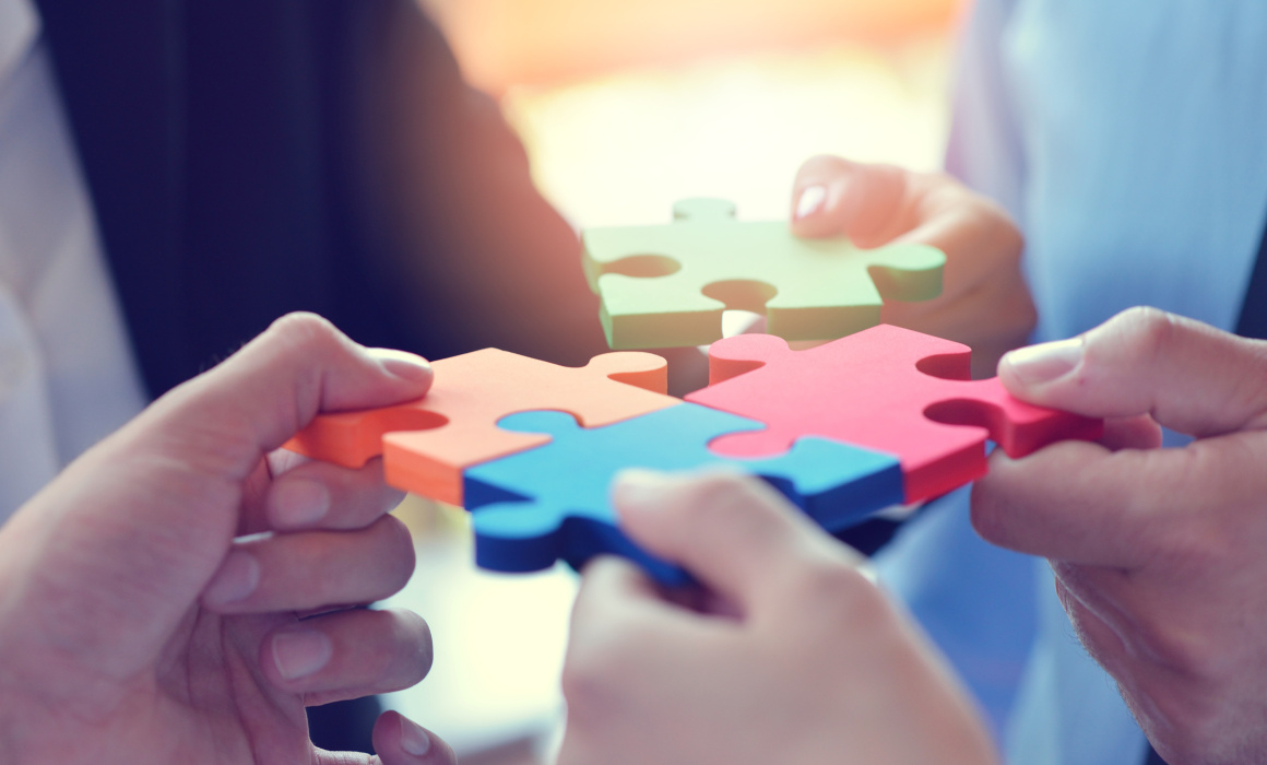 Mehrere Personen setzen gemeinsam vier bunte Puzzleteile zusammen.
